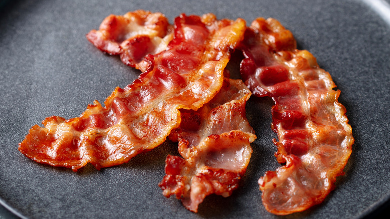 Three strips of crispy bacon on a sleek black plate
