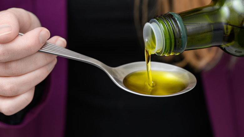 Extra virgin olive oil pouring from a bottle to a metal spoon held by a person's hand