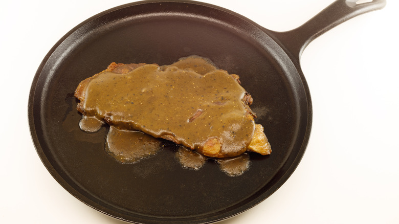 A ham steak covered in red eye gravy on a black skillet