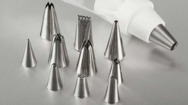 An assortment of metal piping tips with an icing bag in the background
