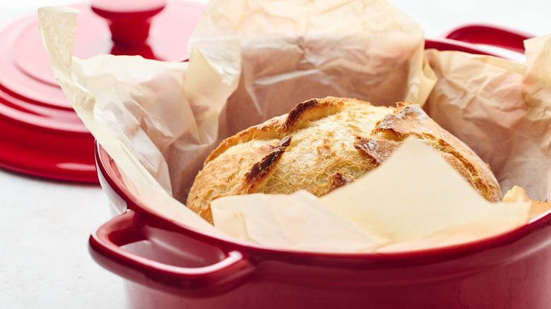 Red enameled Dutch oven with a loaf of artisan-style bread inside