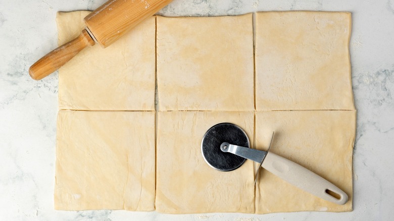 Pastry cutter on top of dough with straight lines cut through it