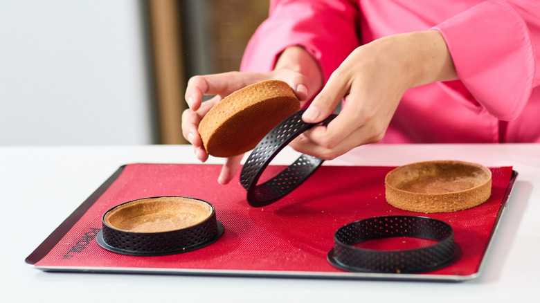Baker taking tarts out of tart rings on a lined baking sheet