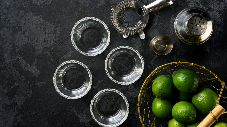 Salt-rimmed glasses, ingredients, and cocktail tools