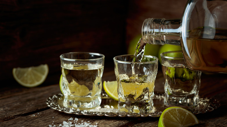 A person pours shots of tequila, which are surrounded by salt and lime wedges
