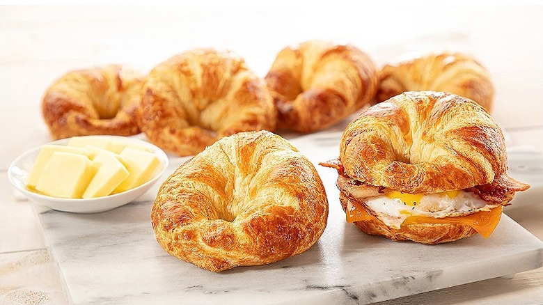 6 golden croissants on a slab, with a small plate of butter next to them