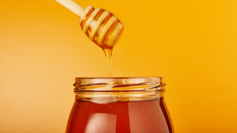A honey dipper is suspended above a jar of honey