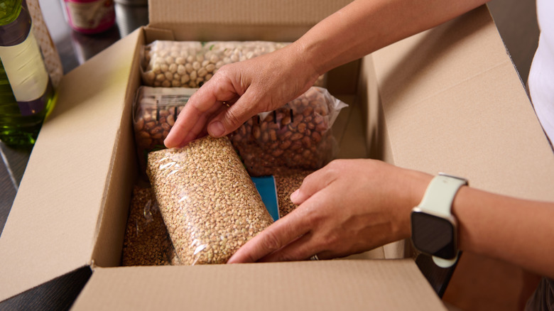 A person unpacks dried groceries from a cardboard box