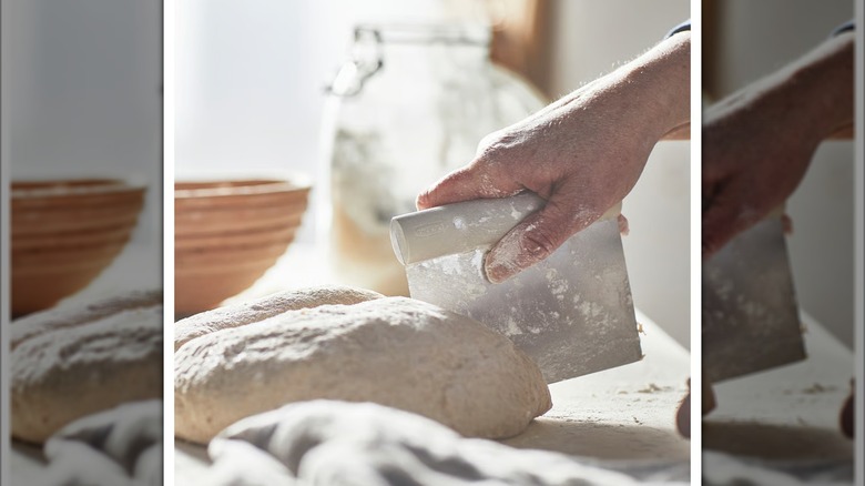 Hand using dough cutter to cut dough on floury surface