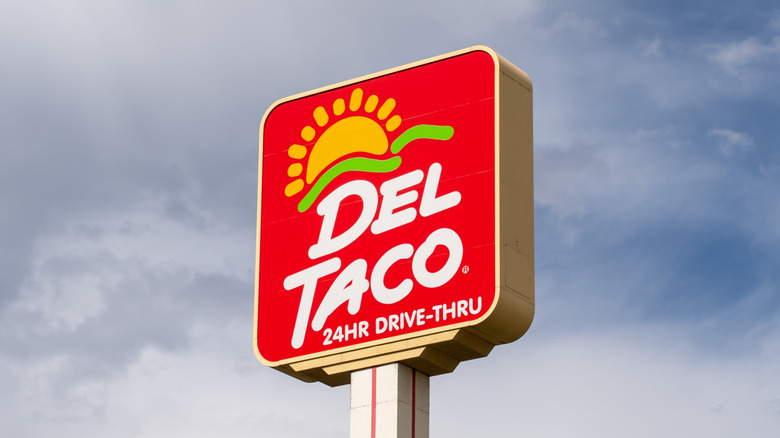 A Del Taco sign is seen against a slightly cloudy sky