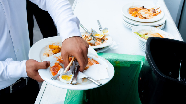 A waiter disposes of uneaten food at a buffet