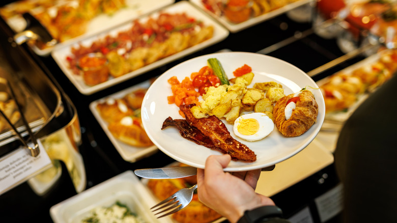 A person holds a plate of breakfast food at a buffet