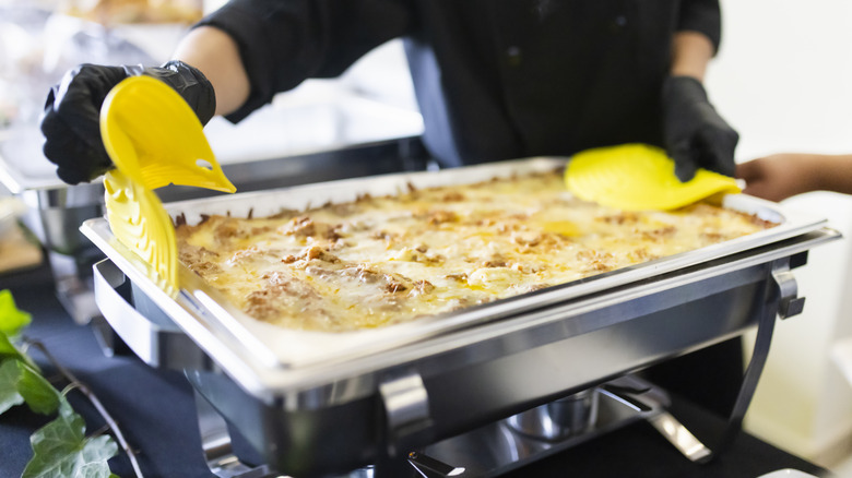 A cook puts a fresh tray of food down at a buffet
