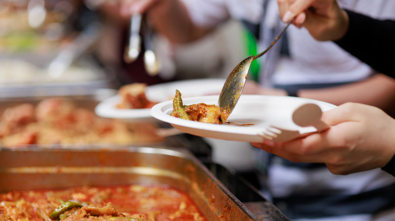 A person spoons food onto their plate at a buffet