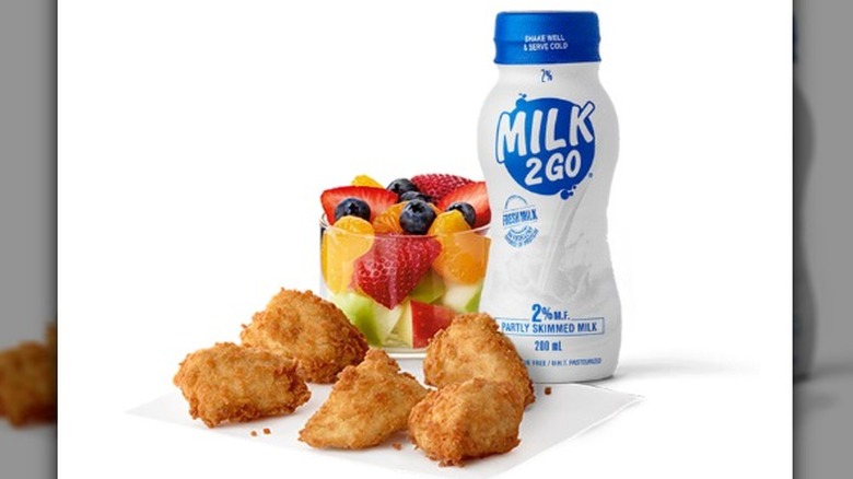Five Chick-Fil-A nuggets, a fruit cup, and bottle of milk against a white background
