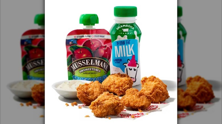 A KFC kids meal with five chicken nuggets, Musselman's unsweetened applesauce, milk, and a dipping sauce against a white background