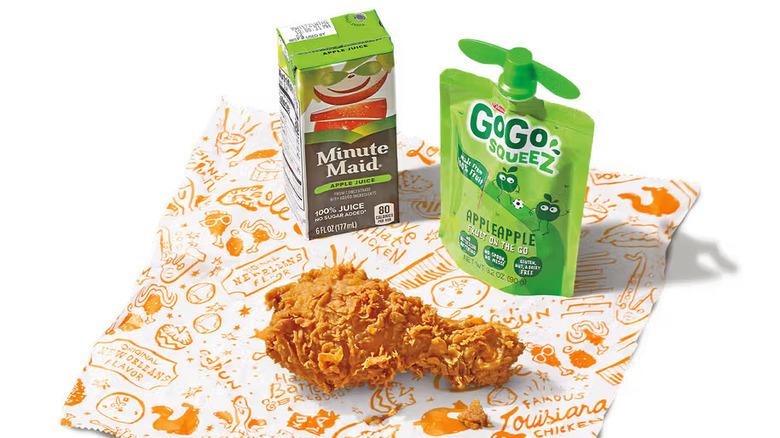 A fried chicken drumstick, Gogo Squeez applesauce, and apple juice on a Popeyes wrapping paper