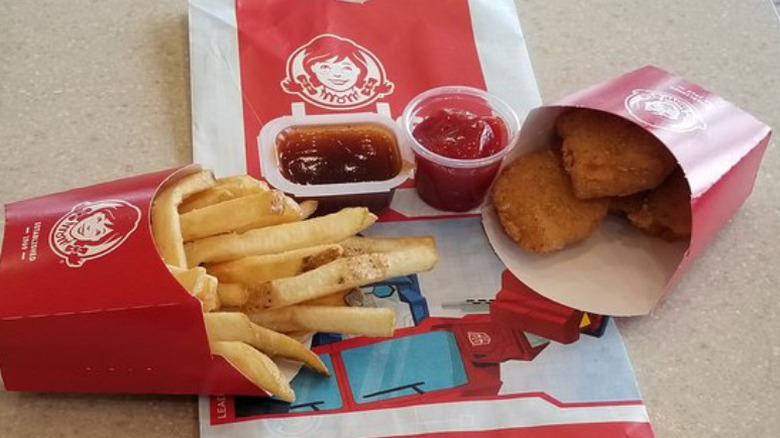A Wendy's kids' meal with fries, BBQ sauce, ketchup, and four chicken nuggets laid out on a table top
