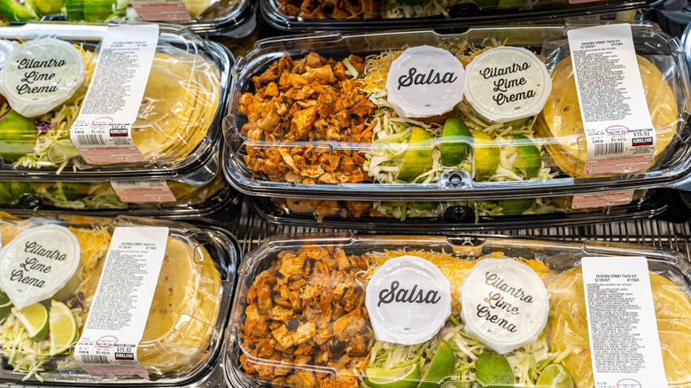 Plastic containers of Costco taco kits arranged on a wire rack at the store