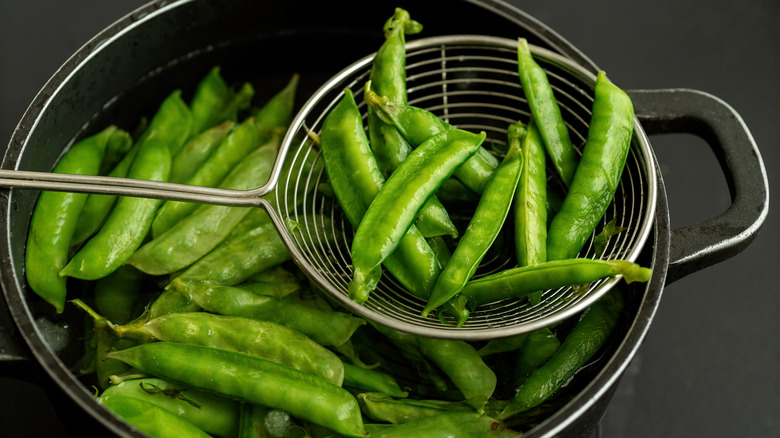 Blanched pea pods in a pot, with a colander
