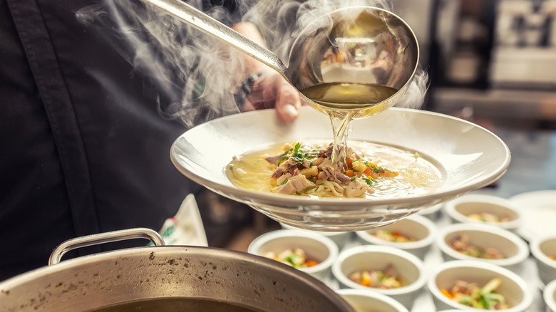 Pouring broth over chicken noodle soup