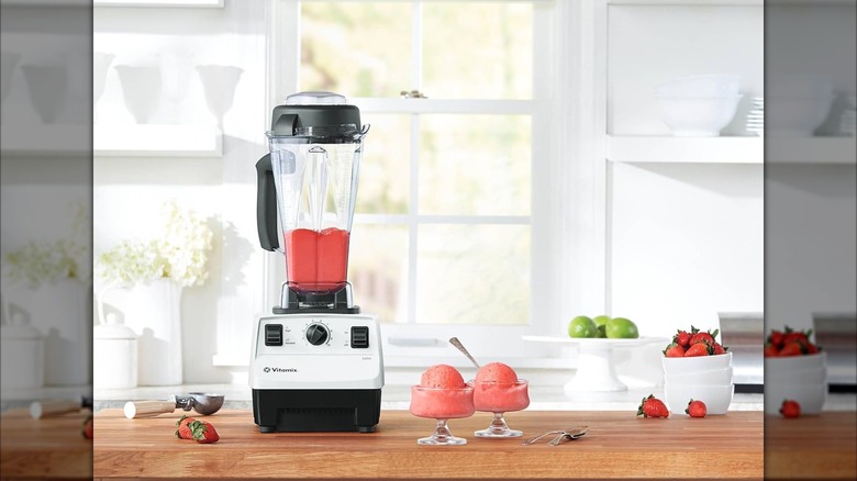 A Vitamix 5200 filled with a reddish blended liquid, with two dessert dishes containing the same
