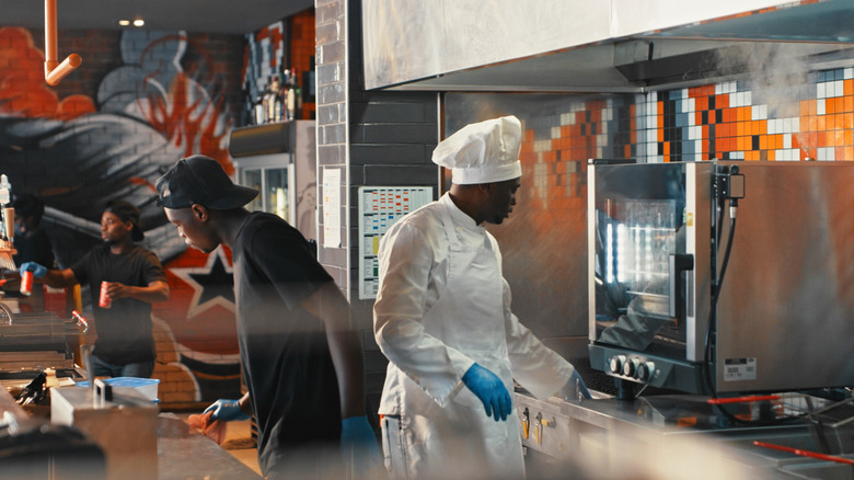 Black men cooking in a commercial open kitchen with a colorful backdrop