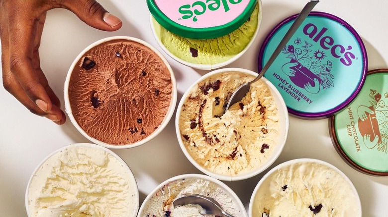 overhead shot of open pints of alec's ice cream styled with lids, a hand reaching