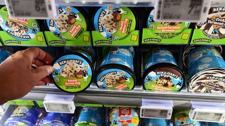close-up of a hand selecting a pint of ben & jerry's from the freezer case in a grocery store
