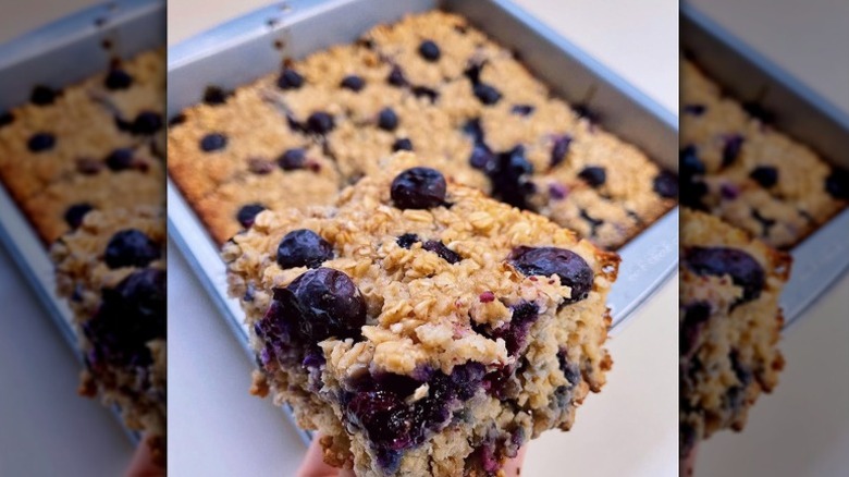 Closeup of a baked oat breakfast bar with blueberries and a tray of oat bars in the background
