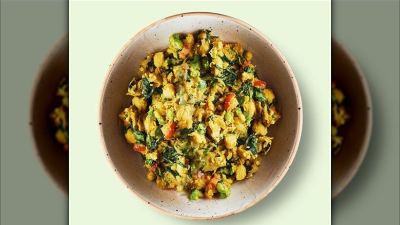 Overhead view of a bowl of chickpea scrambled enough to look like eggs with green veggies mixed in