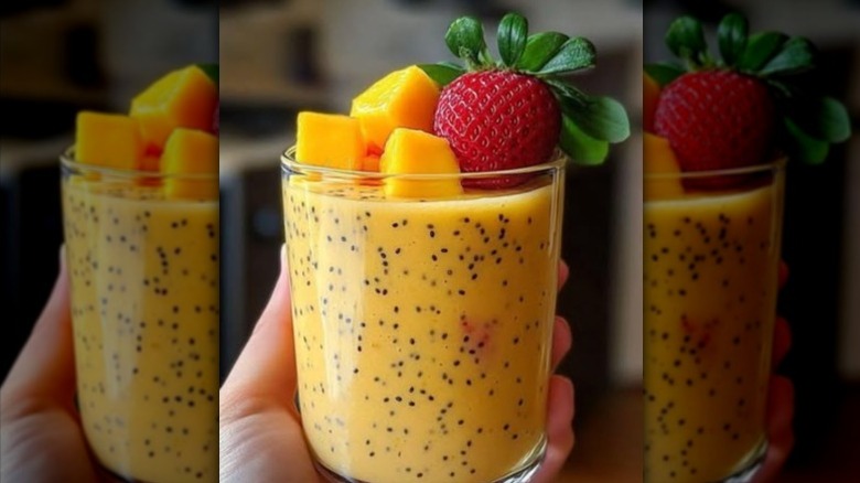 Closeup of a mango smoothie in a glass with visible chia seeds and mangoes and strawberries on top