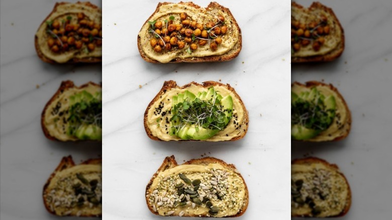 Three different hummus toasts with various plant-based toppings on a white counter