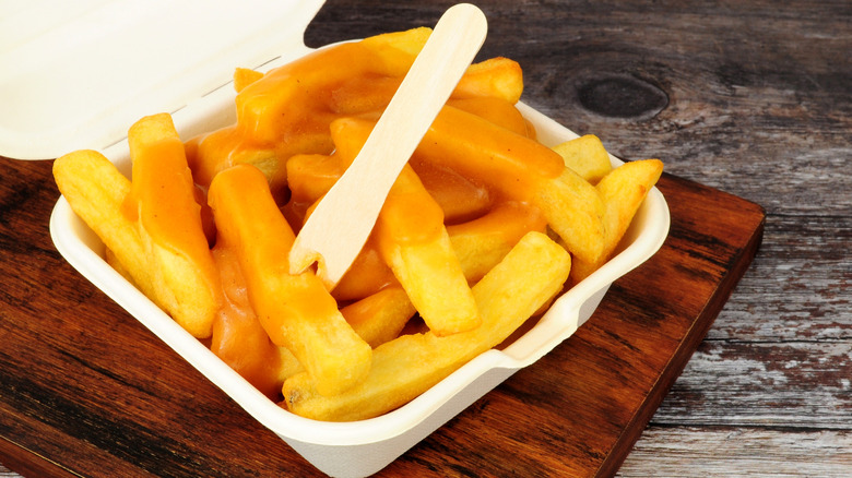 Chips topped with curry sauce in a takeout box with a wooden fork