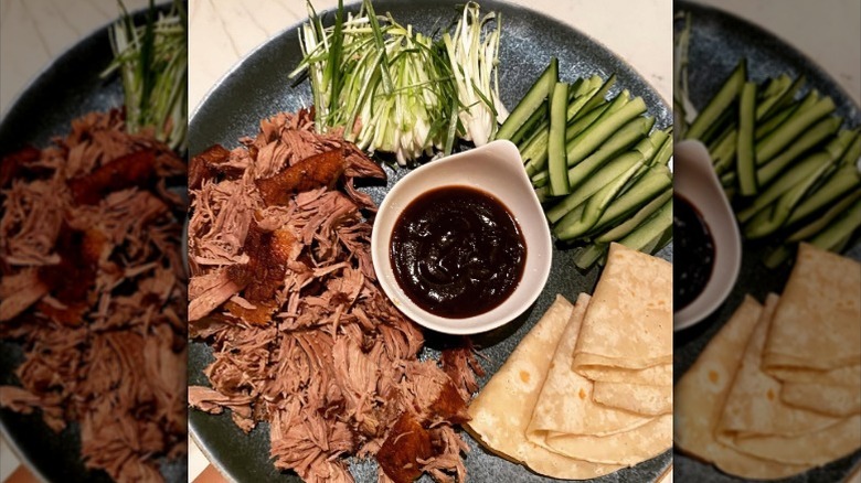 Crispy aromatic duck with hoisin sauce, pancakes, cucumbers, and spring onions on a plate