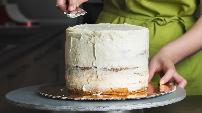 A baker applying a crumb coat on a cake placed on a turntable with a palette knife