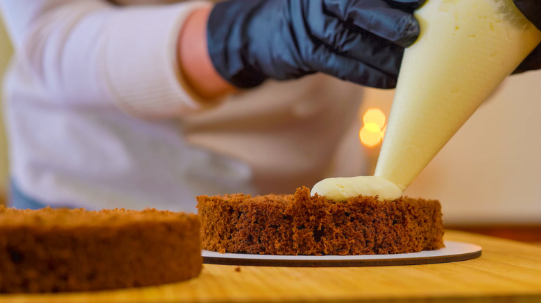 A baker piping frosting on a cake layer