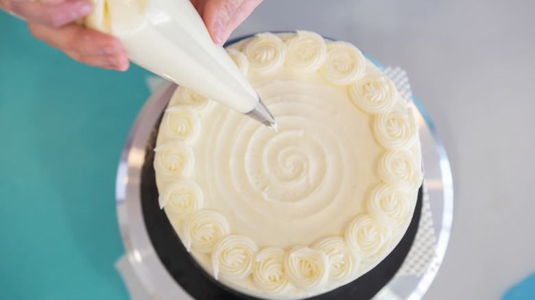 A baker piping a design on a white cake