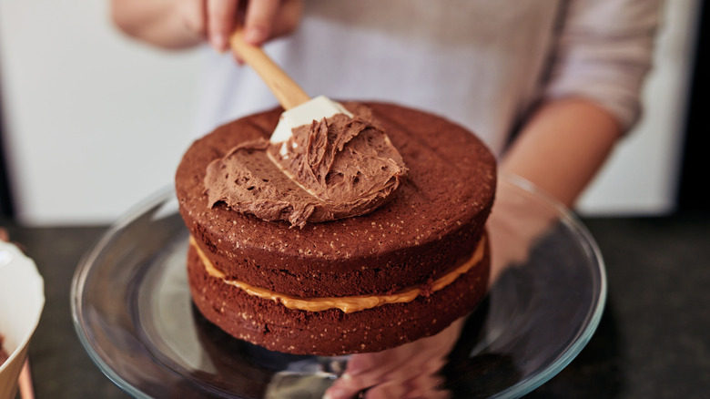 A person spreading out chocolate frosting on top of a chocolate cake