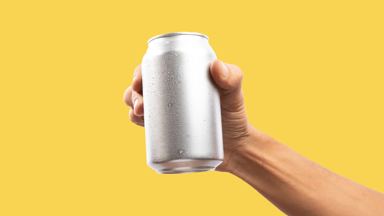 A hand holds an aluminum can on a yellow background