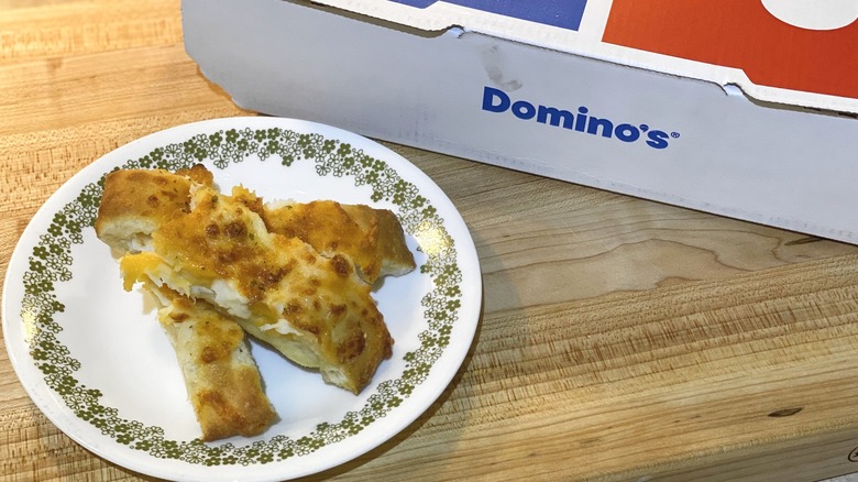 A Domino's breadstick box next to a plate with breadsticks