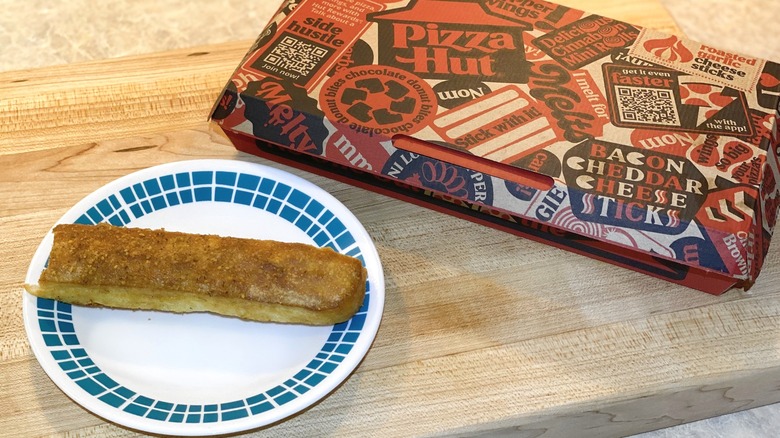 A Pizza Hut breadstick box next to a plate with a breadstick on it