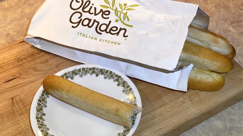 A bag of Olive Garden breadstick next to a plate with a breadstick