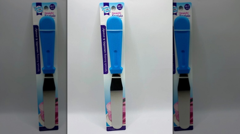 A Baked With Love Straight Spatula leaning against a white wall