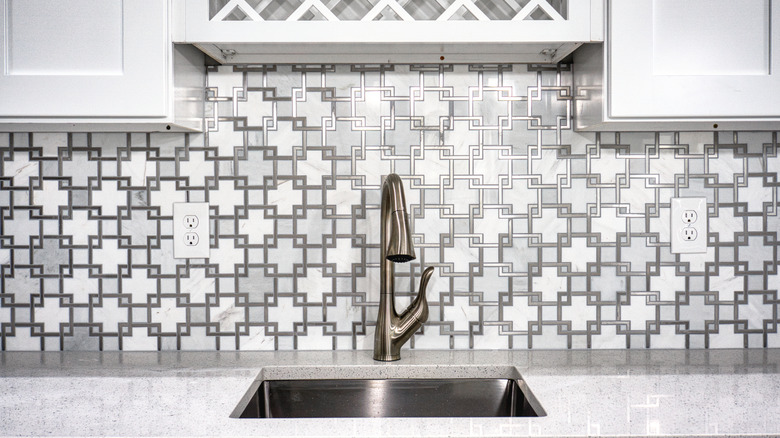 View of kitchen sink with ornate-looking backsplash behind it