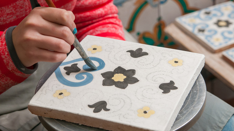 Artist painting white tiles in flowers and swirls