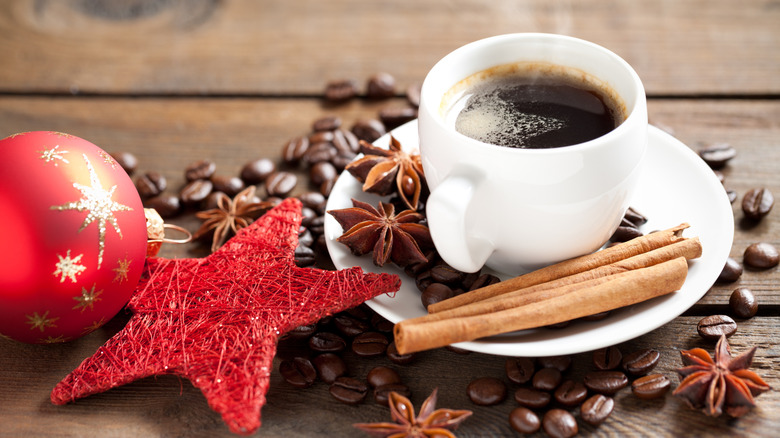 Coffee in a white cup and saucer with beans, star anise, cinnamon sticks, and Christmas baubles