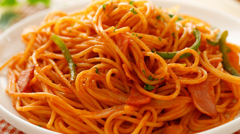Ketchup spaghetti in a white bowl with peppers