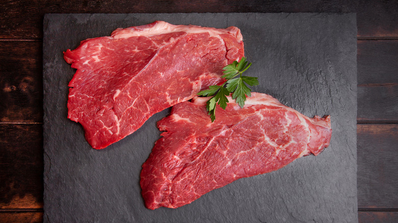Raw minute steak on a black cutting board with garnish