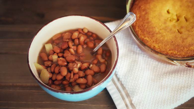 A bowl of pinto beans with onions and cornbread on a wooden surface